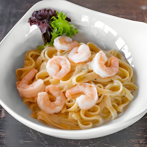Creamy fettuccine pasta with shrimp and a garnish of fresh lettuce in a white bowl.