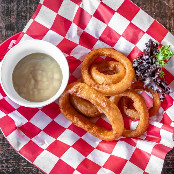 Golden-brown onion rings with a side of dipping sauce and lettuce on red and white checkered paper.