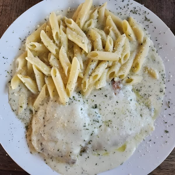 Penne pasta and ravioli covered in creamy white sauce, sprinkled with herbs and pepper.