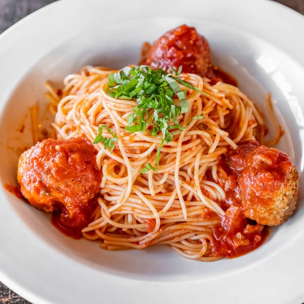 Spaghetti and meatballs with tomato sauce and fresh basil in a white bowl.